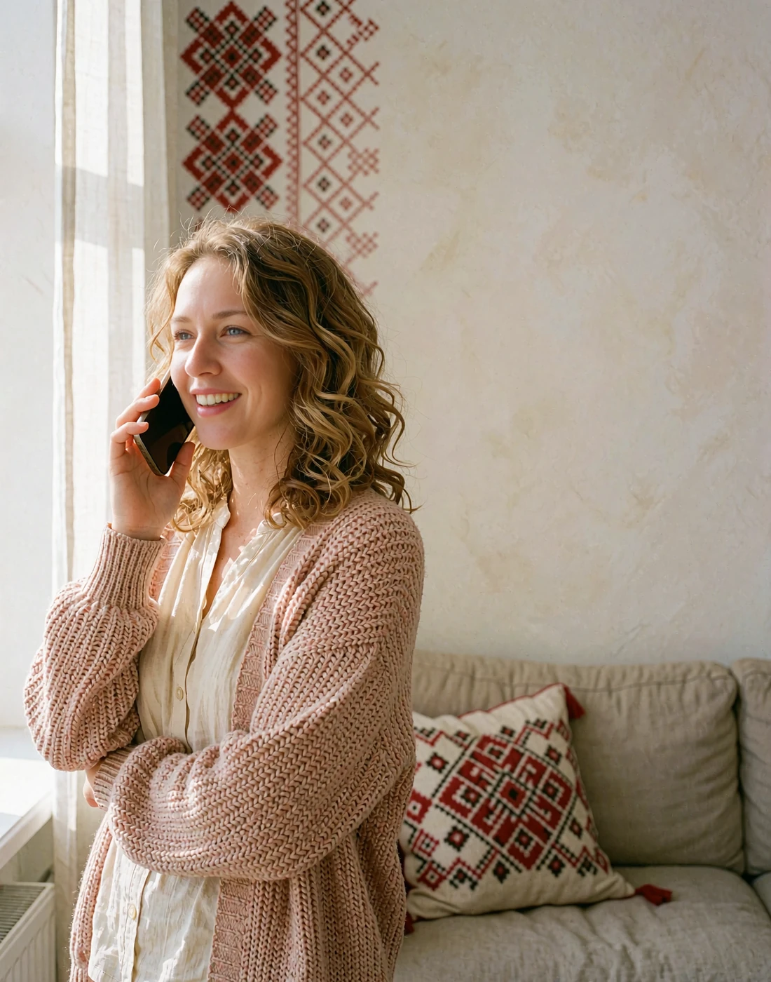 Smiling dark blonde woman on a phone call near a bright window, illustrating cross-language communication on a Slavic dating site